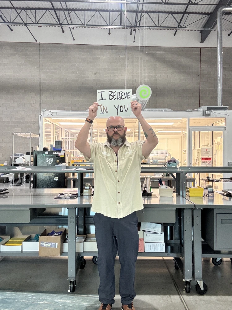 bald man with beard holding sign that says "i believe in you"